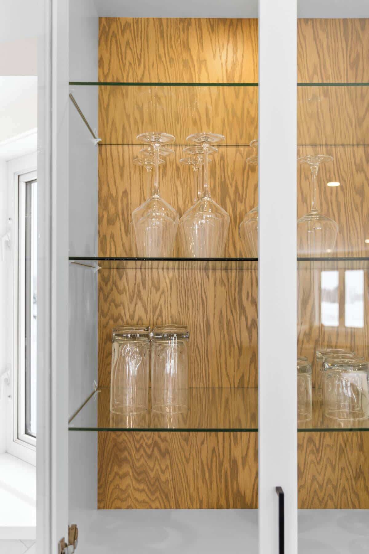 Un mueble de madera con estantes de vidrio que alberga copas de vino y frascos de vidrio transparentes.