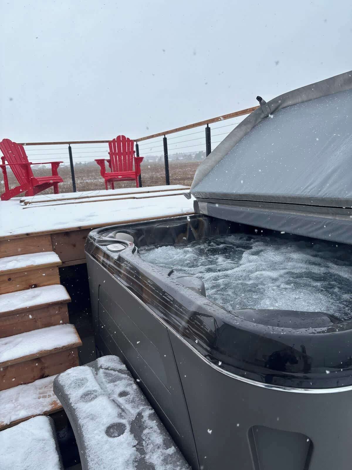 Ein Whirlpool mit Holzterrasse und roten Adirondack-Stühlen.