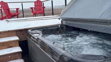Ein Whirlpool mit Holzterrasse und roten Adirondack-Stühlen.