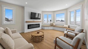 A modern living room with a fireplace, a flat-screen TV, and a cozy seating area with a view of the outdoors.