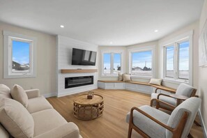 A modern living room with a fireplace, a flat-screen TV, and a cozy seating area with a view of the outdoors. - The Lantern Hill Lookout (North Rustico)