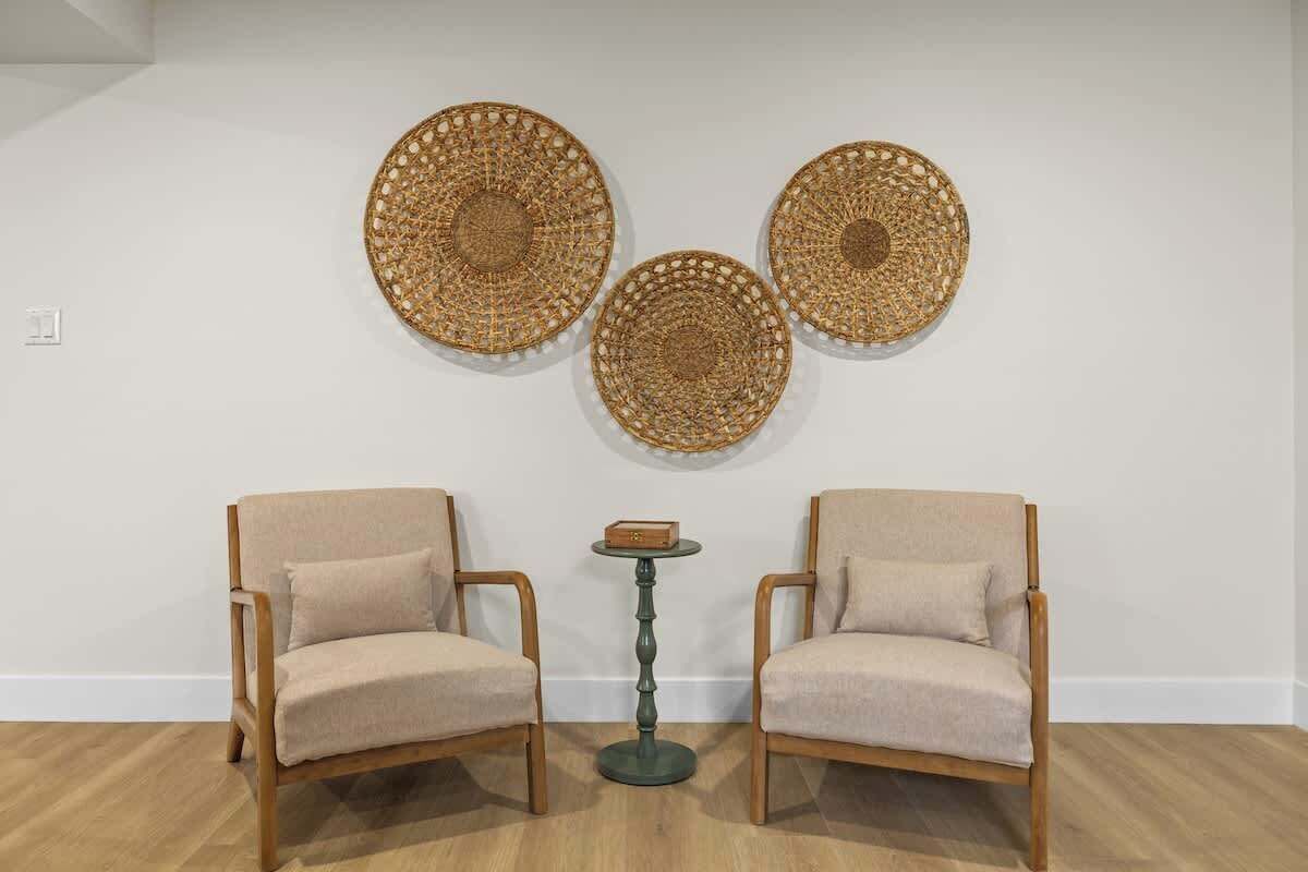 Una habitación con dos sillones de madera, una mesita redonda y tres piezas decorativas tejidas en la pared.