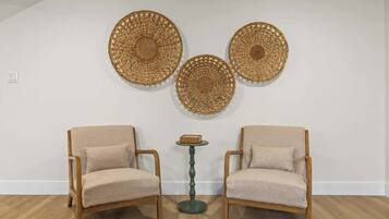Una habitación con dos sillones de madera, una mesita redonda y tres piezas decorativas tejidas en la pared.