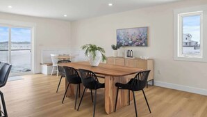 A spacious room with a wooden dining table, black chairs, a potted plant, and a painting on the wall.