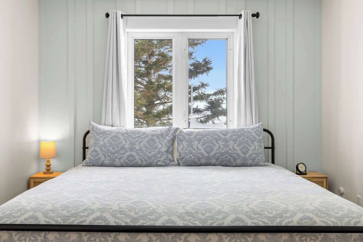 A bed with a patterned bedspread, a window with curtains, and a bedside lamp.