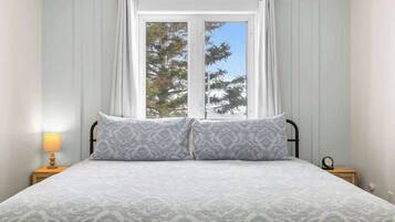 A bed with a patterned bedspread, a window with curtains, and a bedside lamp.