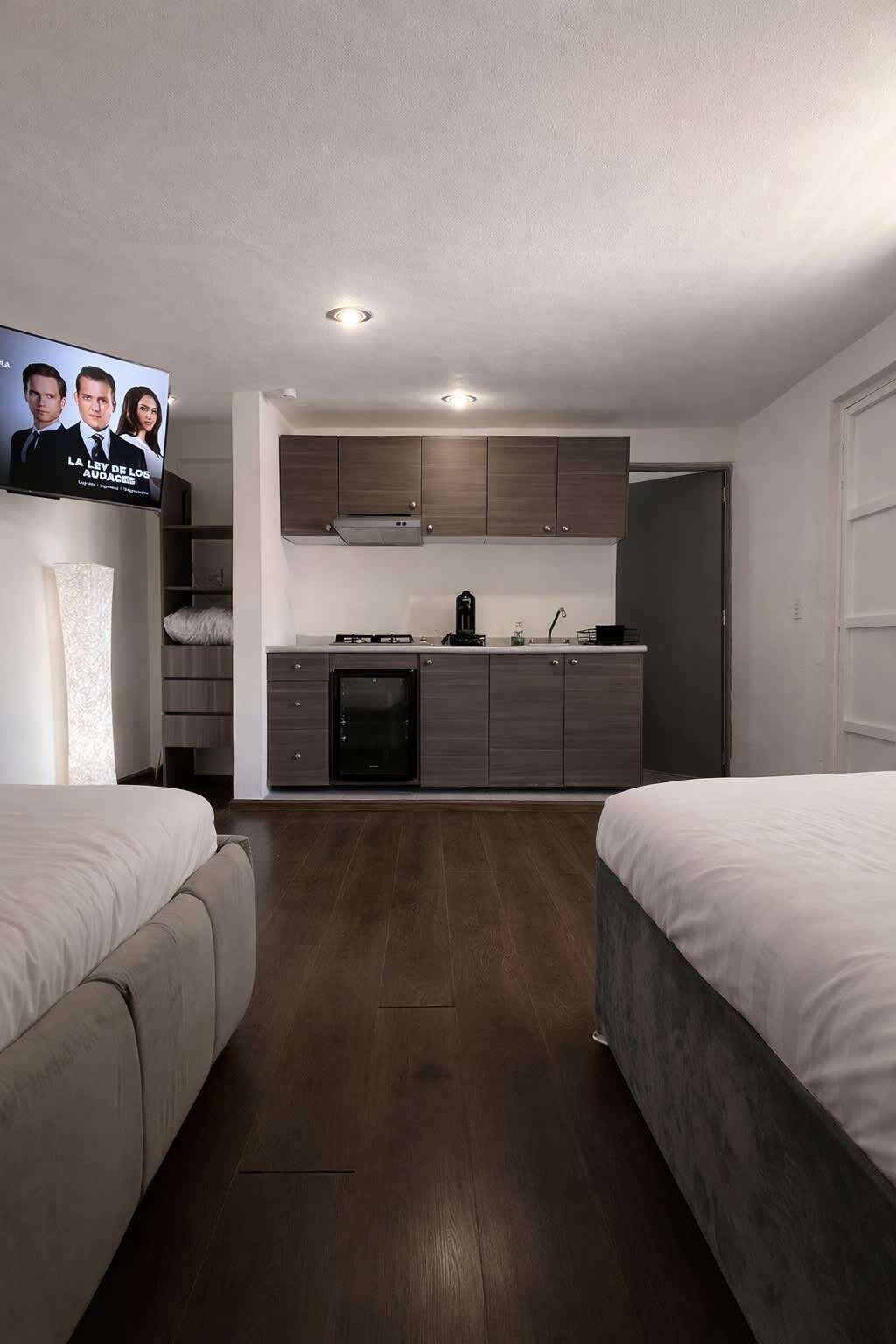 Een moderne hotelkamer met een kitchenette, twee bedden, een televisie en een houten vloer.