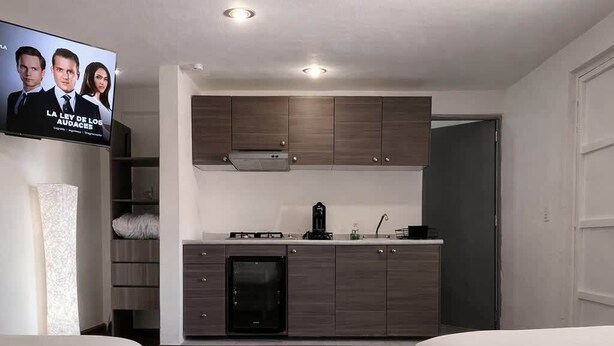Een moderne hotelkamer met een kitchenette, twee bedden, een televisie en een houten vloer.