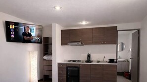 Een moderne hotelkamer met een bed, een televisie, een kitchenette en een badkamer.