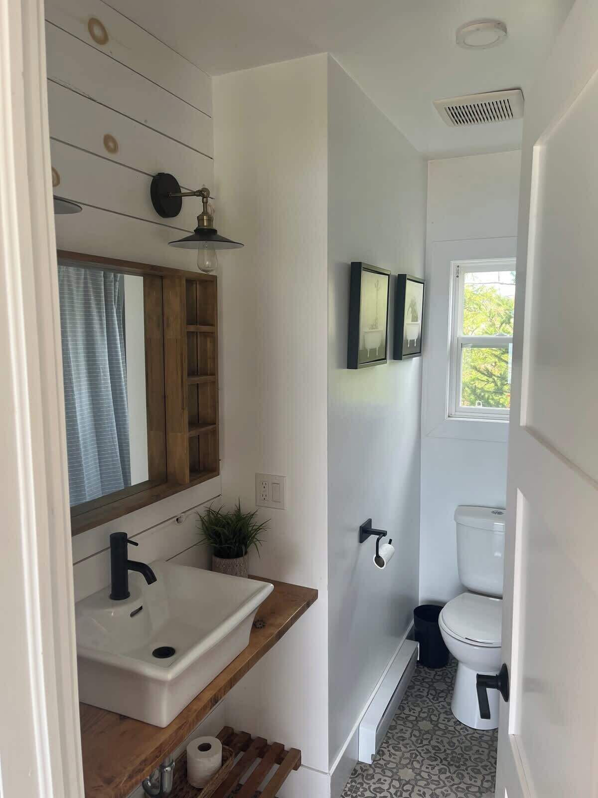 A bathroom with a wooden vanity, a sink, a mirror, a toilet, and a window.