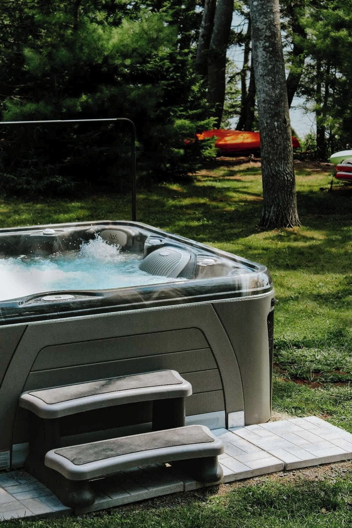 Un bain à remous avec des marches menant à celui-ci, entouré d’herbe et d’arbres.