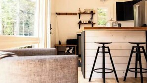 Eine Küche mit Holzbalken, einer Bar mit Hockern, einem Kühlschrank und einem Fenster mit Blick auf Bäume.