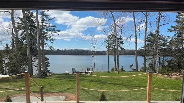 Eine Terrasse mit roten Stühlen mit Blick auf einen See, umgeben von Bäumen und einem Seilzaun.