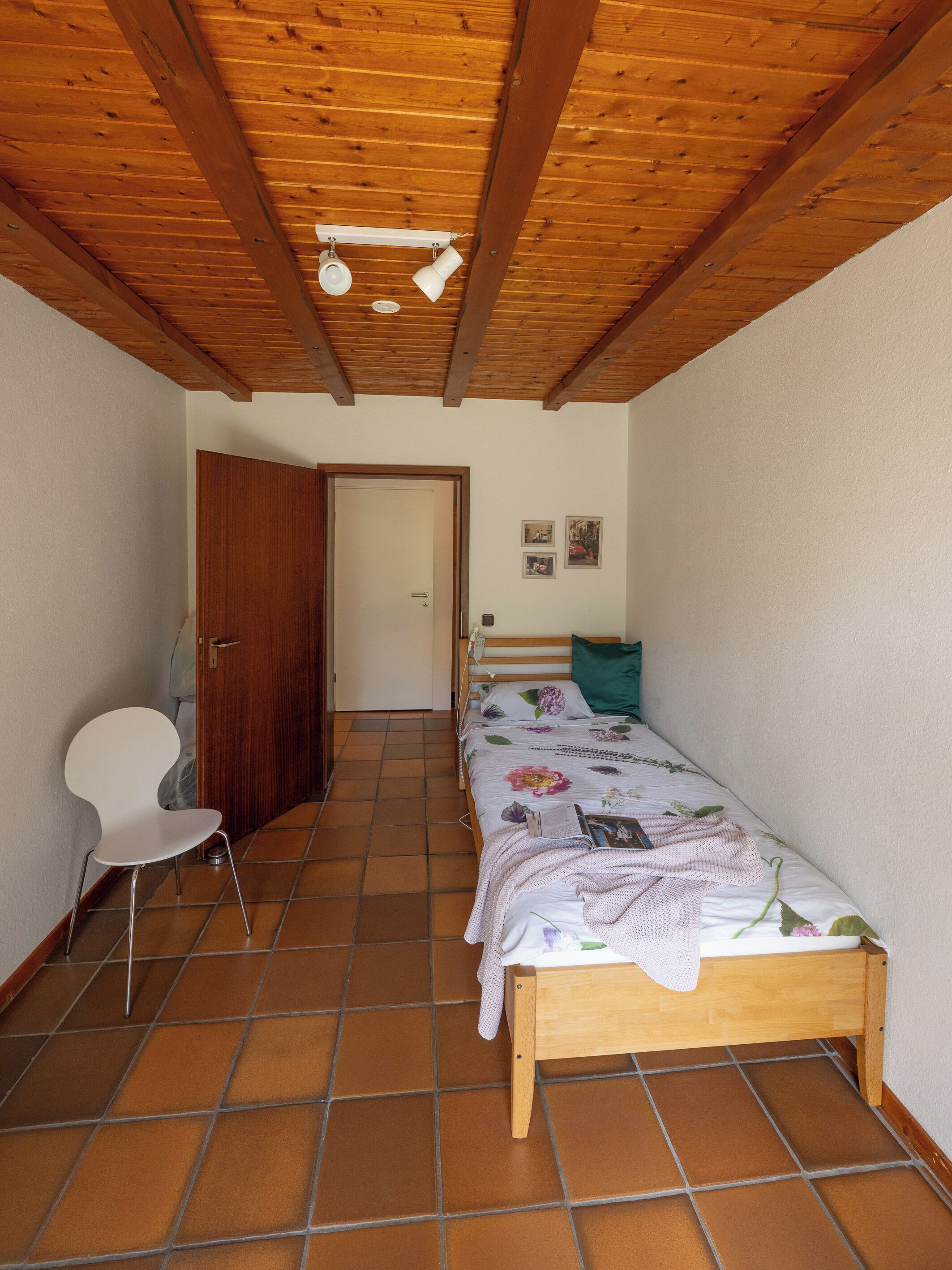 A bedroom with a wooden bed, a white chair, and a door leading to another room.