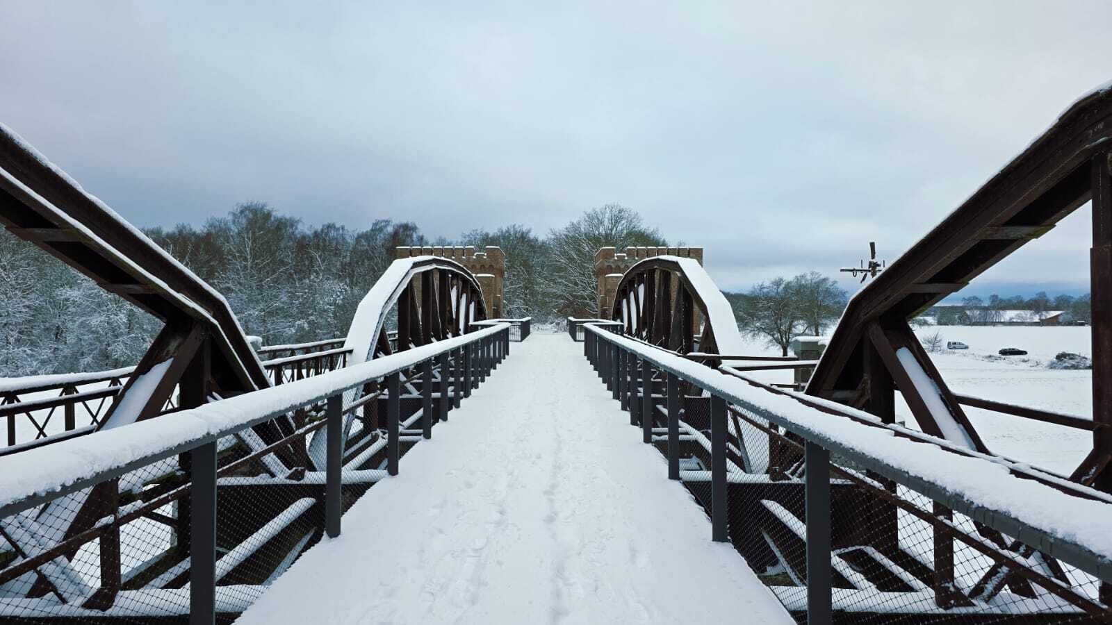 Un pont piétonnier enneigé, doté de rampes métalliques et d’un chemin dégagé.