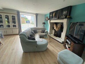 A living room with a sectional sofa, a fireplace, a television, and a view through a large window.