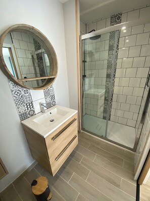 A bathroom with a wooden vanity, a round mirror, a glass shower enclosure, and patterned tiles.