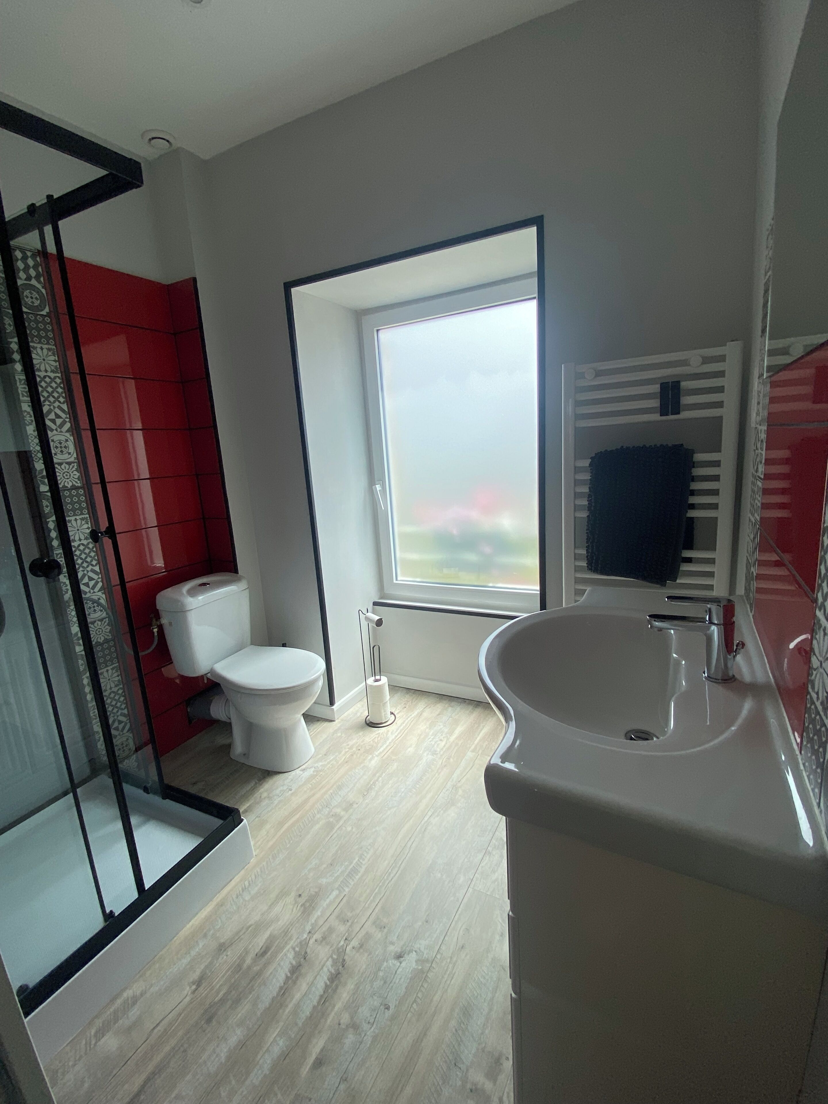 A bathroom with a shower, toilet, sink, and a large window.