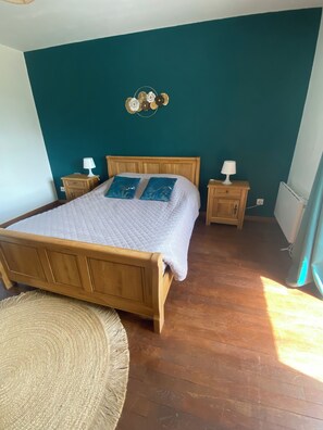 A bedroom with a wooden bed, two bedside tables with lamps, a wall clock, and a woven rug.
