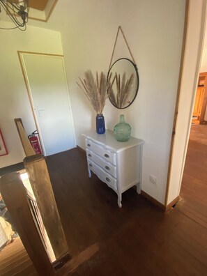 A room with a white dresser, a mirror, and a vase with pampas grass.