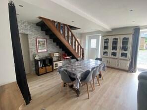 Un comedor con mesa, sillas, una escalera, una zona de cocina y vistas a través de una ventana.