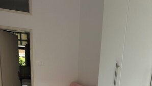 Una habitación con sofá rosa, armario blanco y suelo de baldosas.