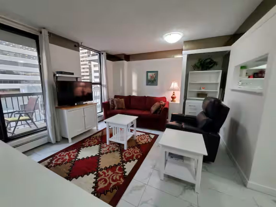 A living room with a red sofa, white coffee table, and a TV on a cabinet. There is a patterned rug on the floor.