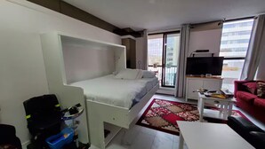 A bedroom with a bed, a TV, a red sofa, and a balcony with a view. - City Center, Murphy Bed & Kitchen 300 Airport bus. private condo with balcony (Calgary)