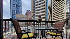 A balcony with two chairs and a table, overlooking a cityscape with modern buildings. - City Center, Murphy Bed & Kitchen 300 Airport bus. private condo with balcony (Calgary)