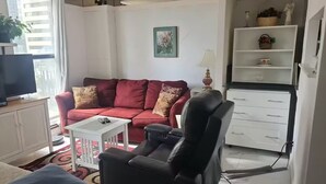 A living room with a red sofa, a black chair, a TV, a small table, and a cabinet with shelves. - City Center, Murphy Bed & Kitchen 300 Airport bus. private condo with balcony (Calgary)