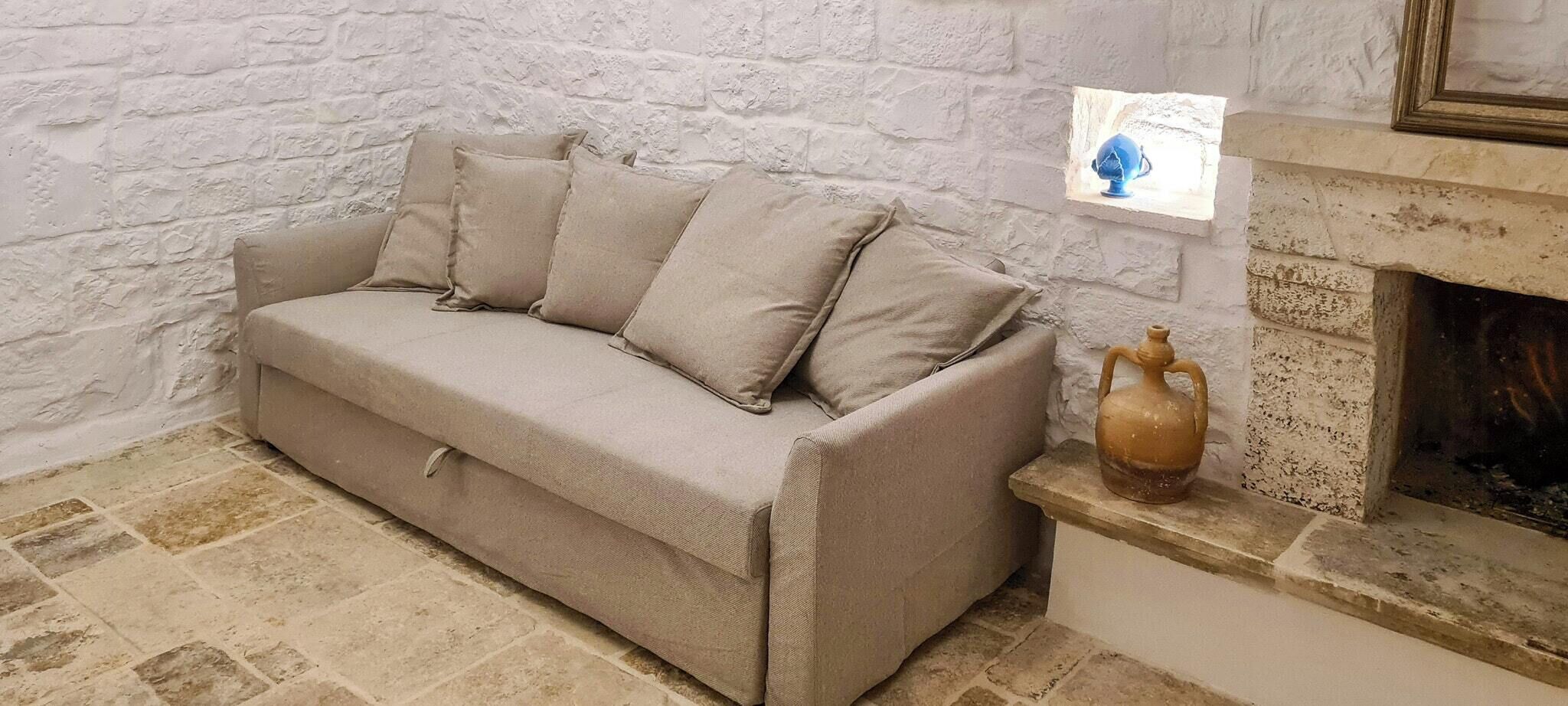 Un divano beige appoggiato a un muro di mattoni bianchi, un piccolo vaso su una mensola e un camino.