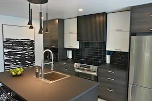 A modern kitchen with a central island, stainless steel appliances, and dark cabinetry.