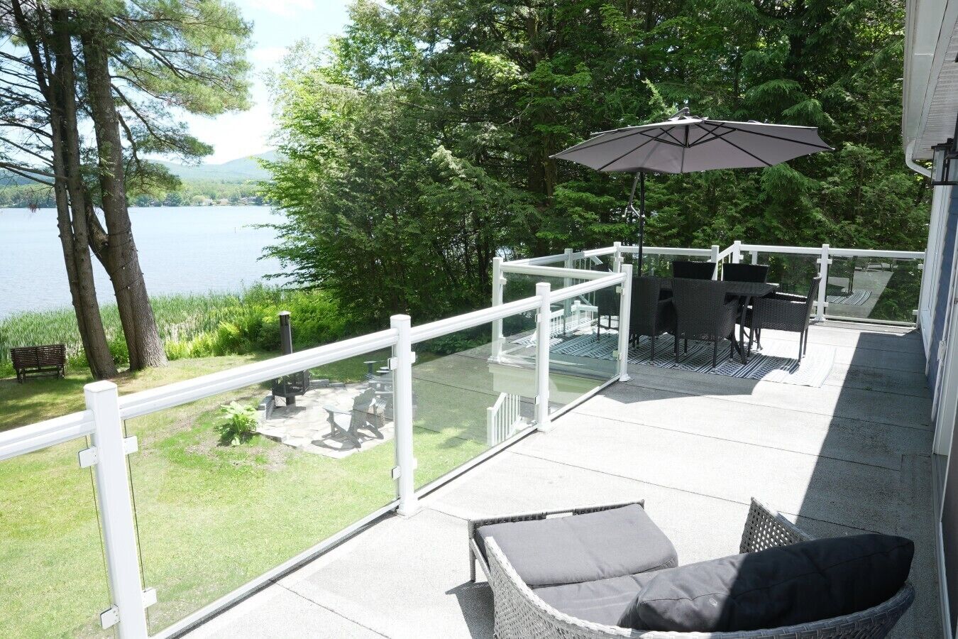 Een terras met buitenmeubilair, een glazen balustrade en uitzicht op een meer.