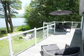 Eine Terrasse mit Gartenmöbeln, einer Glasbrüstung und Blick auf einen See.