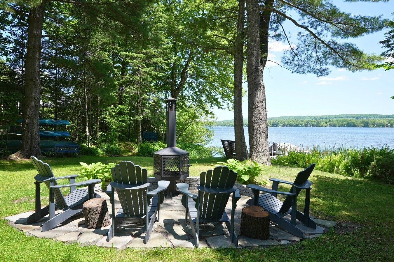Een terras aan het meer met Adirondack stoelen, een houtkachel en uitzicht op het water.