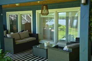 Ein Zimmer mit einer Couch, einem Glastisch und Blick auf eine Terrasse und Wasser.