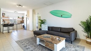 A modern living room with a sofa, coffee table, and a surfboard decoration on the wall.