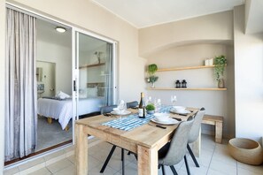 Een eethoek met een houten tafel, stoelen en een bankje. Er is een schuifdeur naar een slaapkamer.