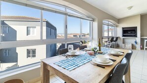 A dining area with a wooden table set for four, large windows, and a flat-screen TV mounted on the wall.