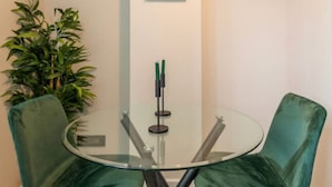 Una habitación con una mesa de vidrio, dos sillas verdes, una planta en maceta y un cuadro en la pared.