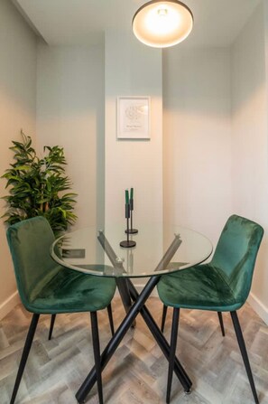 A room with a glass table, two green chairs, a potted plant, and a framed picture on the wall. - Luxury One Bed Apartment Foreshore Cape Town (Cape Town)
