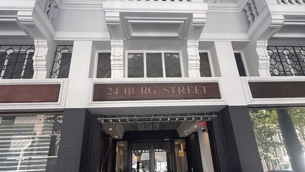 Entrada de un edificio con un letrero que dice '24 Burg Street', que presenta un acceso moderno con puertas de vidrio y fachada blanco y negro.