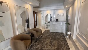 Zona de recepción con suelo de mármol, mostrador de recepción, sofá marrón y arte abstracto en la pared.