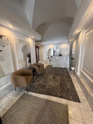 A reception area with a marble floor, a reception desk, a brown sofa, and abstract wall art. - Modern City-center Studio in Historic Venice House (Cape Town)