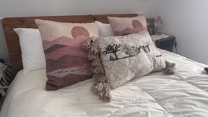 Una cama con ropa blanca, un cabecero de madera y almohadas decorativas con estampados.