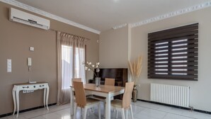 A dining area with a table, chairs, a vase with flowers, a TV, and a window with blinds. - Sea and City Views Apartment in Villa Zina (Rethymno)