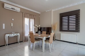 A dining area with a table, chairs, a vase with flowers, a TV, and a window with blinds. - Sea and City Views Apartment in Villa Zina (Rethymno)