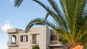 A two-story building with a balcony, surrounded by a well-maintained lawn and a palm tree. - Sea and City Views Apartment in Villa Zina (Rethymno)