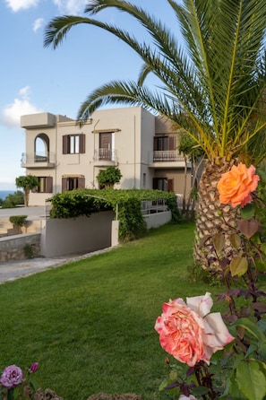A two-story building with a balcony, surrounded by a well-maintained lawn and a palm tree. - Sea and City Views Apartment in Villa Zina (Rethymno)