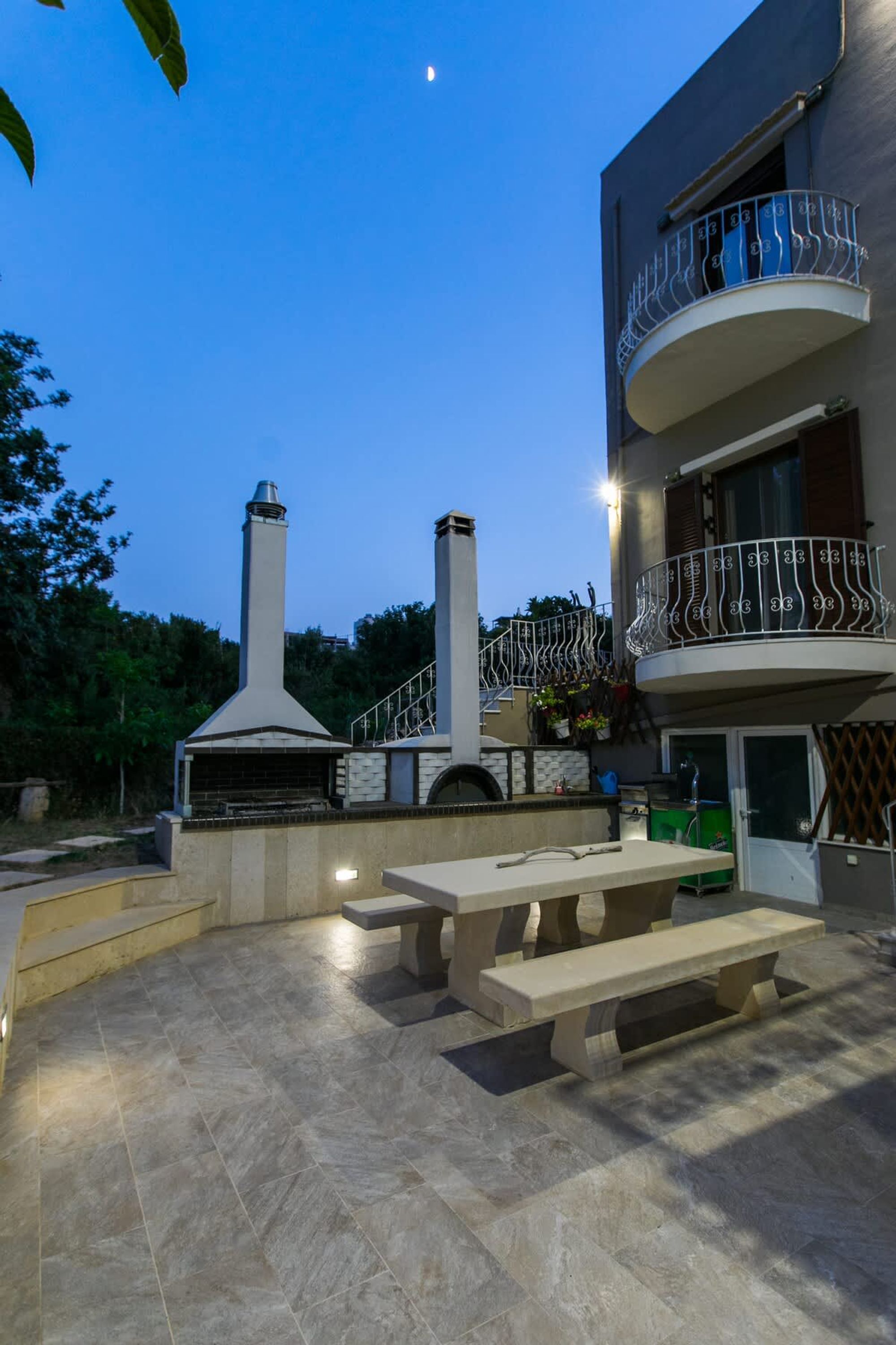 Une terrasse extérieure dotée d’un sol carrelé en pierre, d’un barbecue intégré et d’un espace détente avec des bancs.